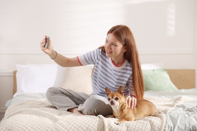 Photo of Smiling teenage girl taking selfie by smartphone and dog on bed at home