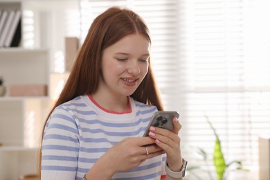 Photo of Smiling teenage girl using smartphone at home