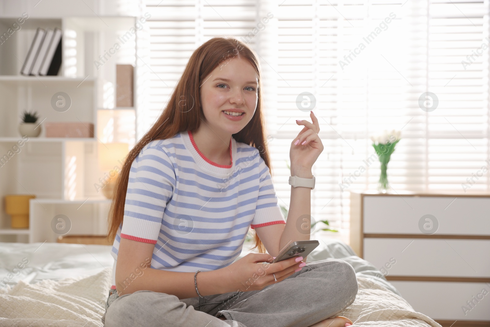Smiling teenage girl with smartphone on bed at home Photo of Smiling teenage girl with smartphone on bed at home