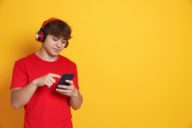 Photo of Teenage boy in headphones using smartphone on yellow background. Space for text