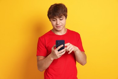 Photo of Teenage boy using smartphone on yellow background