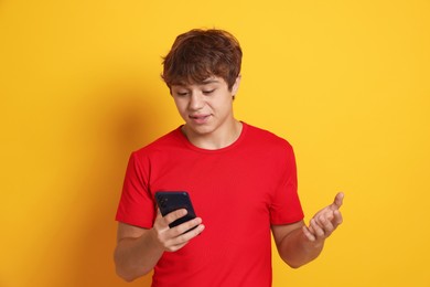 Photo of Teenage boy having videocall by smartphone on yellow background