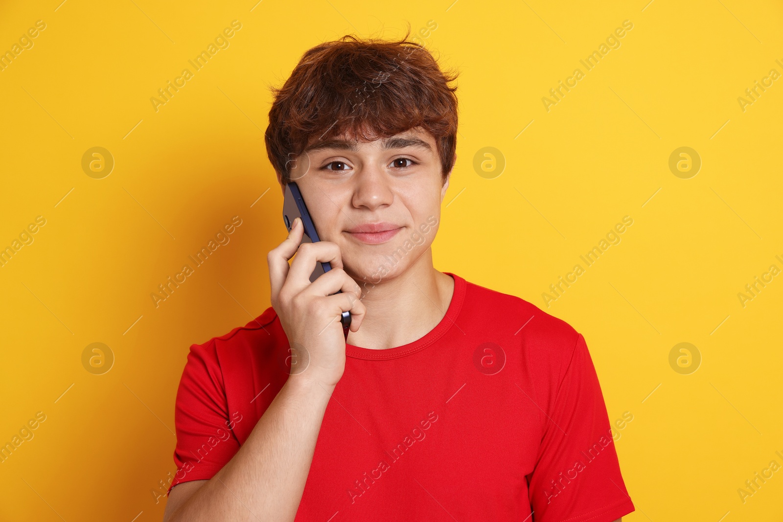 Portrait of teenage boy talking by smartphone on yellow background Photo of Portrait of teenage boy talking by smartphone on yellow background