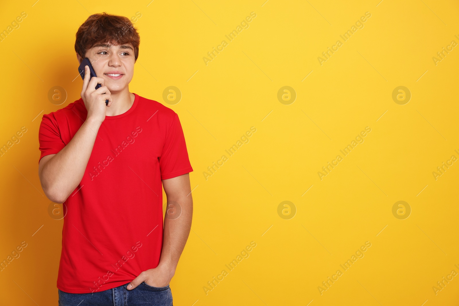 Smiling teenage boy talking by smartphone on yellow background. Space for text Photo of Smiling teenage boy talking by smartphone on yellow background. Space for text