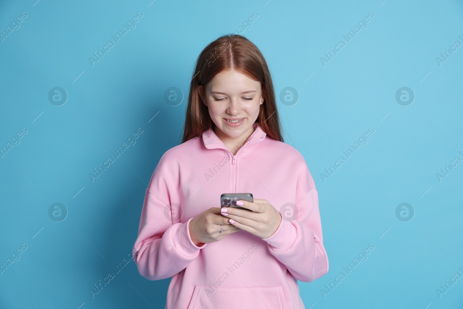 Smiling teenage girl using smartphone on light blue background Photo of Smiling teenage girl using smartphone on light blue background