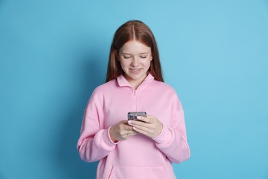 Photo of Smiling teenage girl using smartphone on light blue background