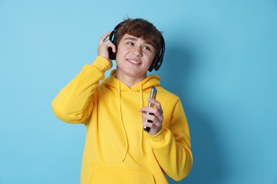 Photo of Smiling teenage boy in headphones with smartphone on light blue background