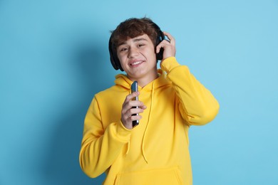 Photo of Smiling teenage boy in headphones with smartphone on light blue background