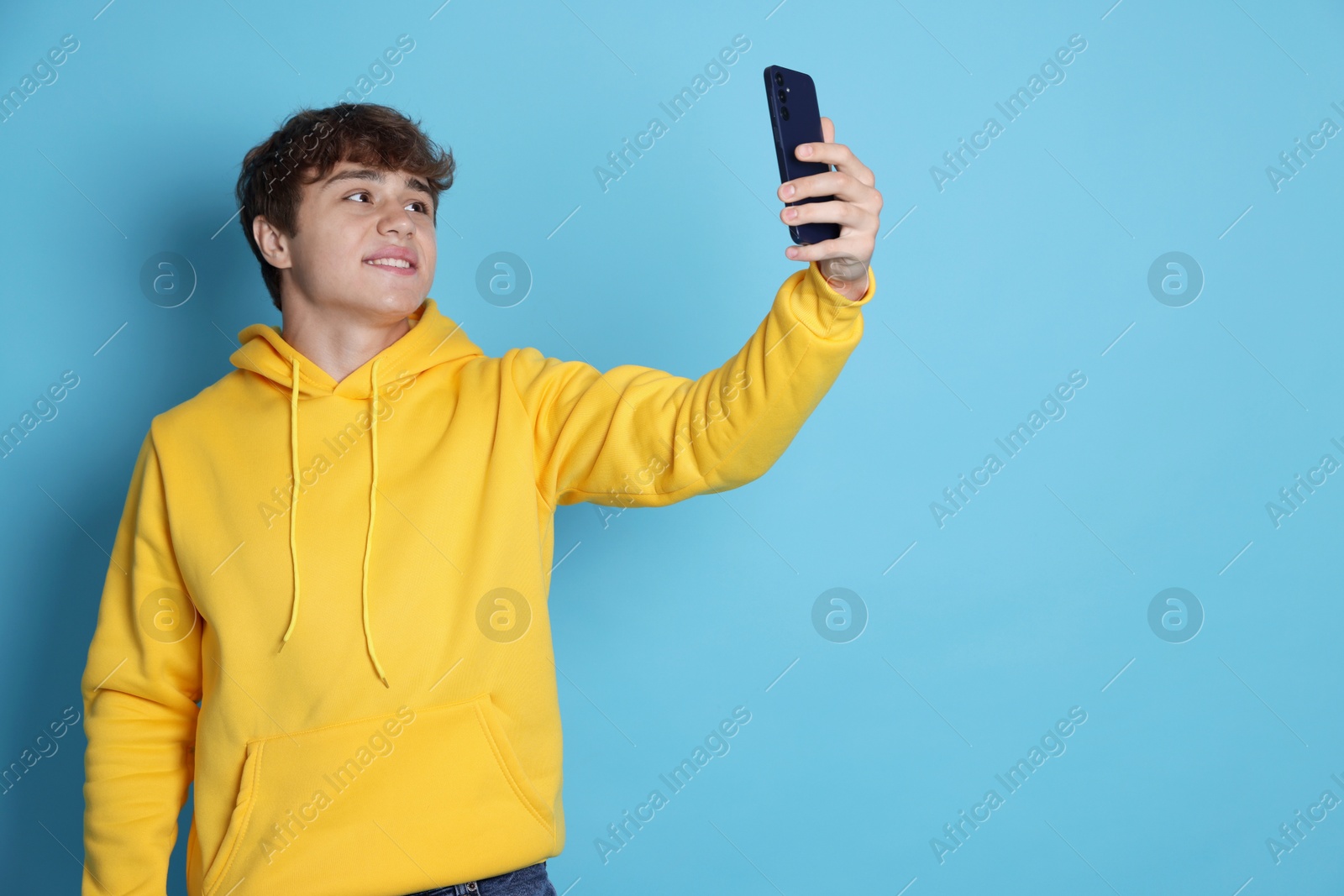 Smiling teenage boy taking selfie by smartphone on light blue background. Space for text Photo of Smiling teenage boy taking selfie by smartphone on light blue background. Space for text