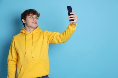 Photo of Smiling teenage boy taking selfie by smartphone on light blue background. Space for text