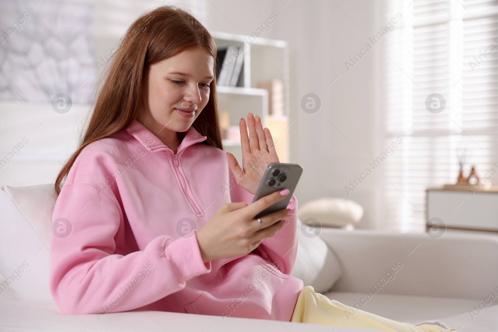 Beautiful teenage girl having videocall by smartphone on sofa at home Photo of Beautiful teenage girl having videocall by smartphone on sofa at home