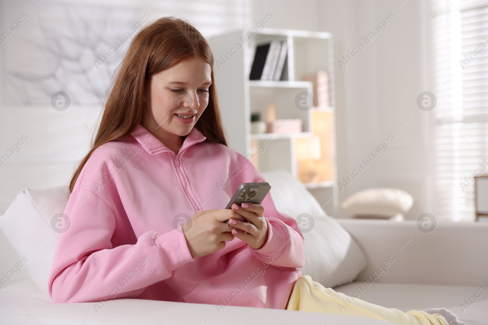 Smiling teenage girl using smartphone on sofa at home Photo of Smiling teenage girl using smartphone on sofa at home