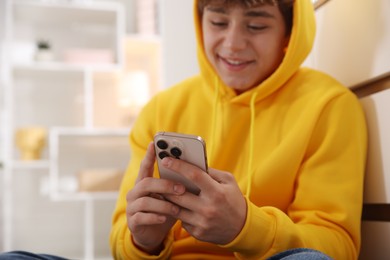 Photo of Smiling teenage boy using smartphone at home