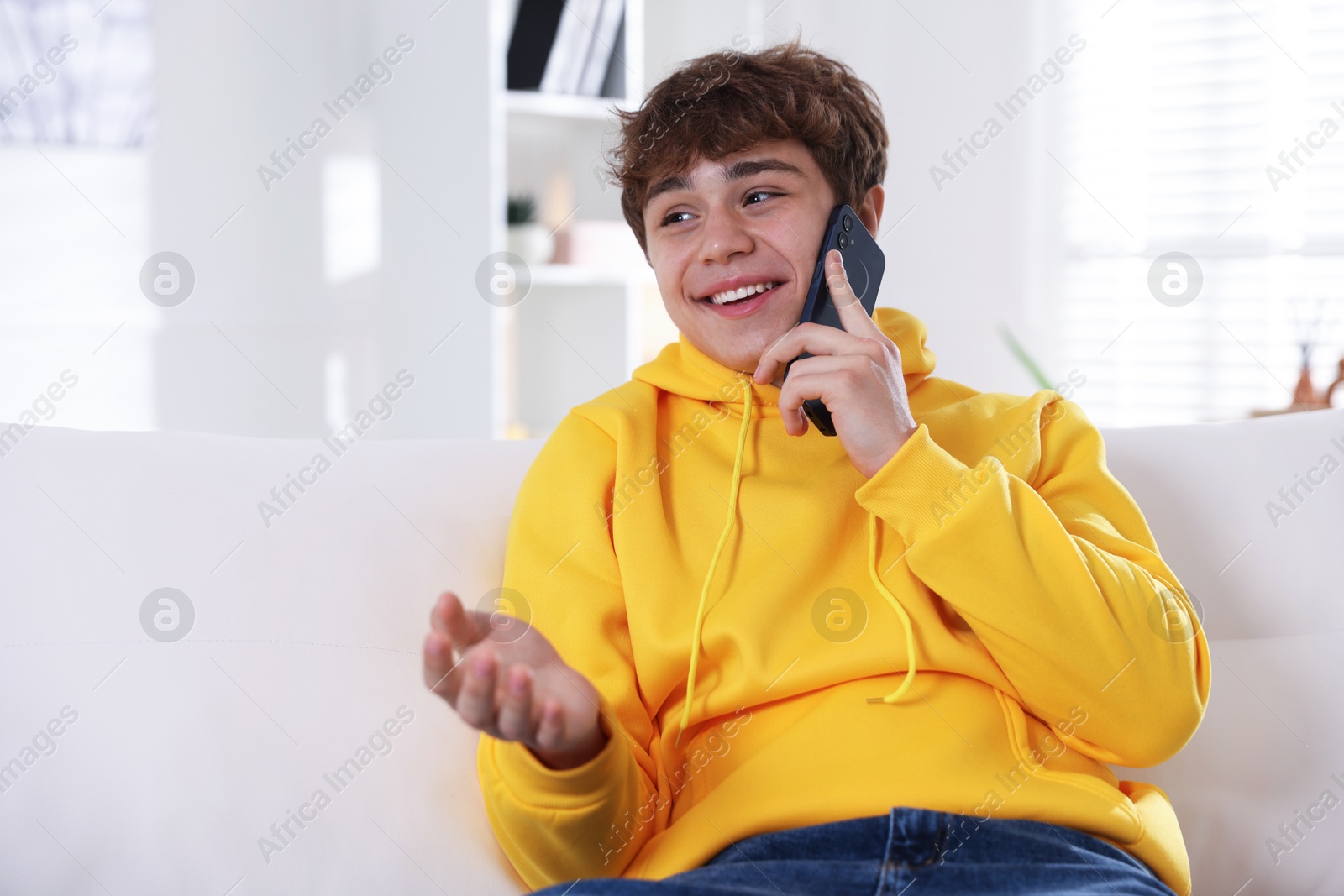 Smiling teenage boy talking by smartphone on sofa at home Photo of Smiling teenage boy talking by smartphone on sofa at home