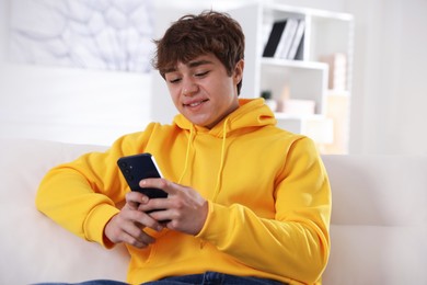 Photo of Smiling teenage boy using smartphone on sofa at home
