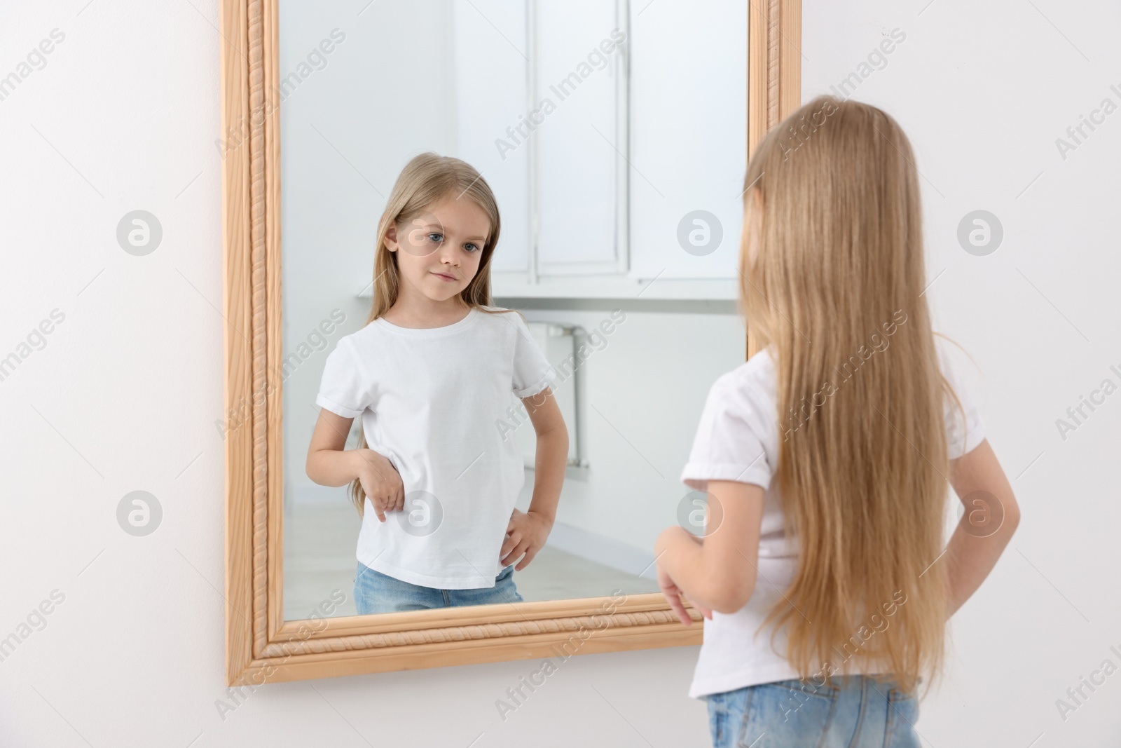 Upset little girl looking at herself in mirror indoors Photo of Upset little girl looking at herself in mirror indoors