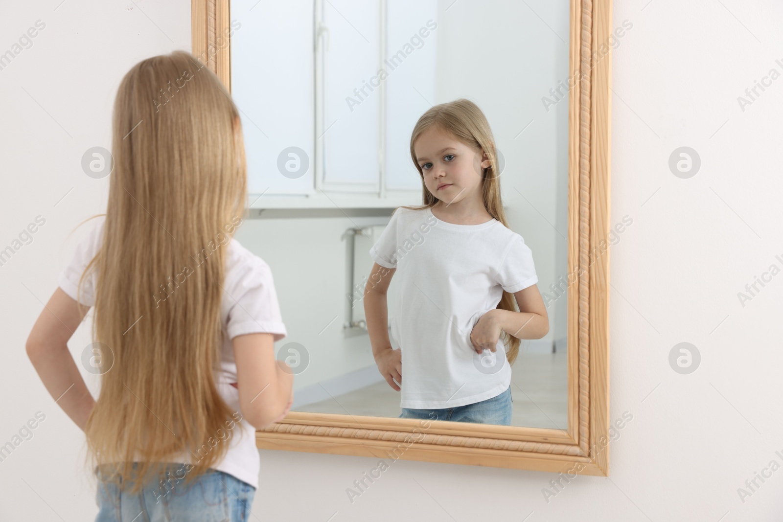 Upset little girl looking at herself in mirror indoors Photo of Upset little girl looking at herself in mirror indoors