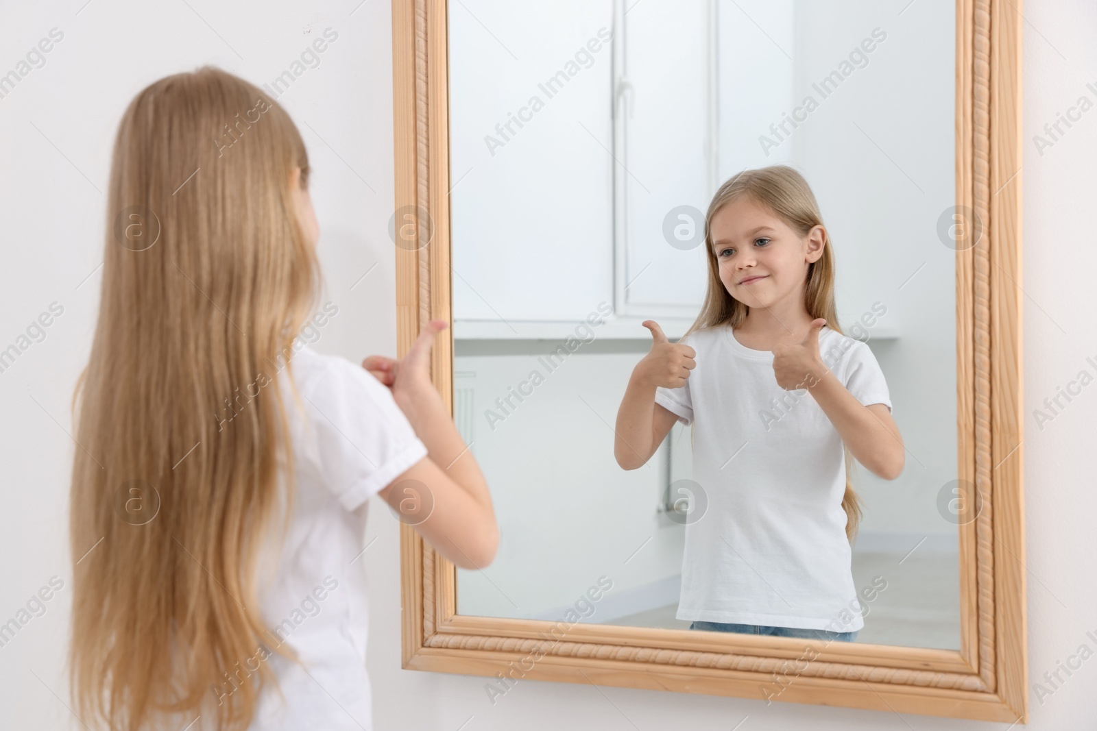 Beautiful little girl showing thumbs up while looking in mirror indoors Photo of Beautiful little girl showing thumbs up while looking in mirror indoors