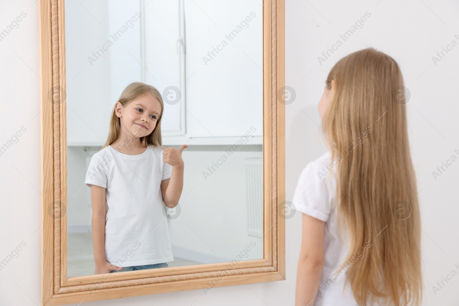 Beautiful little girl showing thumbs up while looking in mirror indoors Photo of Beautiful little girl showing thumbs up while looking in mirror indoors