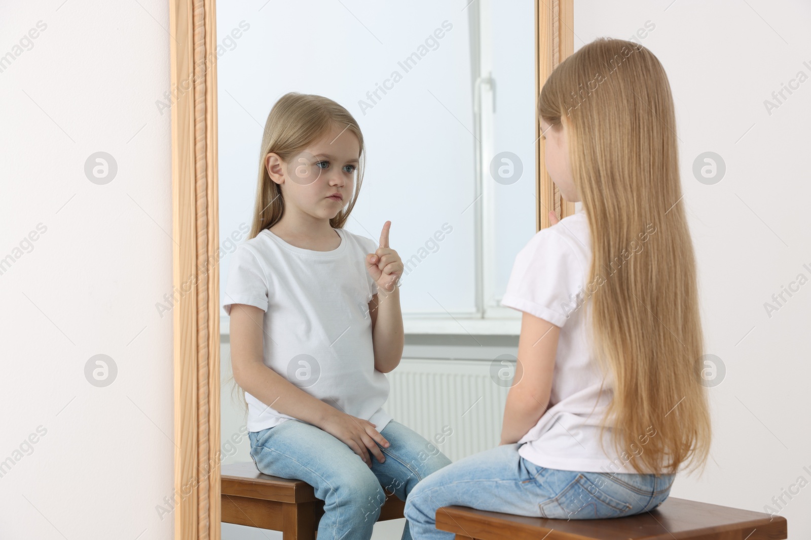 Upset little girl looking at herself in mirror indoors Photo of Upset little girl looking at herself in mirror indoors