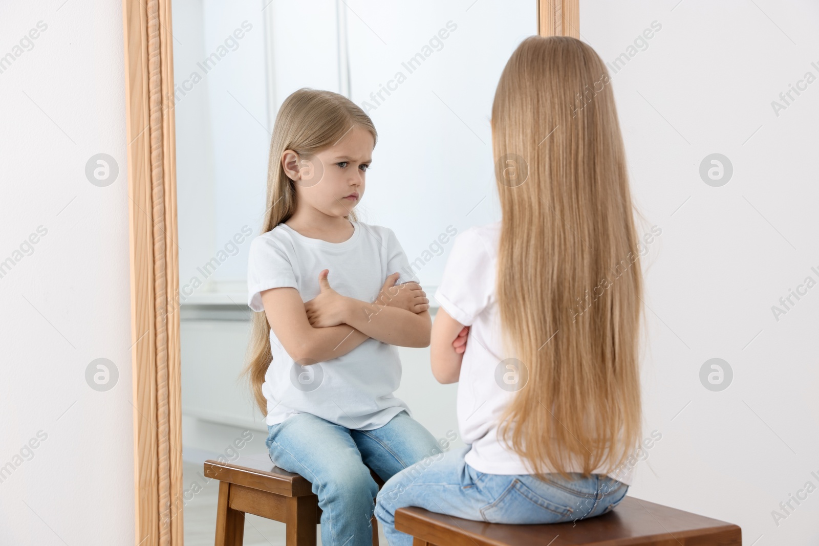 Upset little girl looking at herself in mirror indoors Photo of Upset little girl looking at herself in mirror indoors