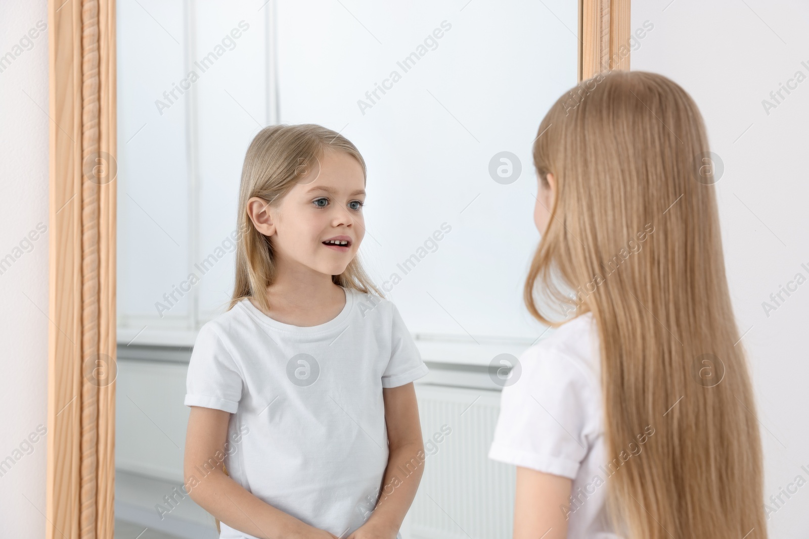 Beautiful little girl looking at herself in mirror indoors Photo of Beautiful little girl looking at herself in mirror indoors