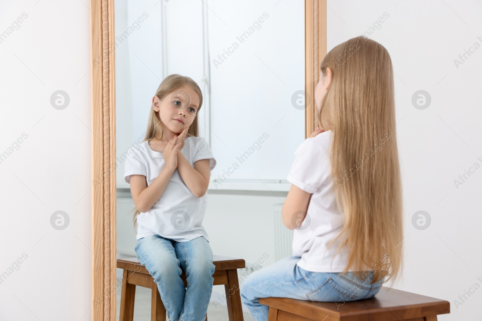 Upset little girl looking at herself in mirror indoors Photo of Upset little girl looking at herself in mirror indoors