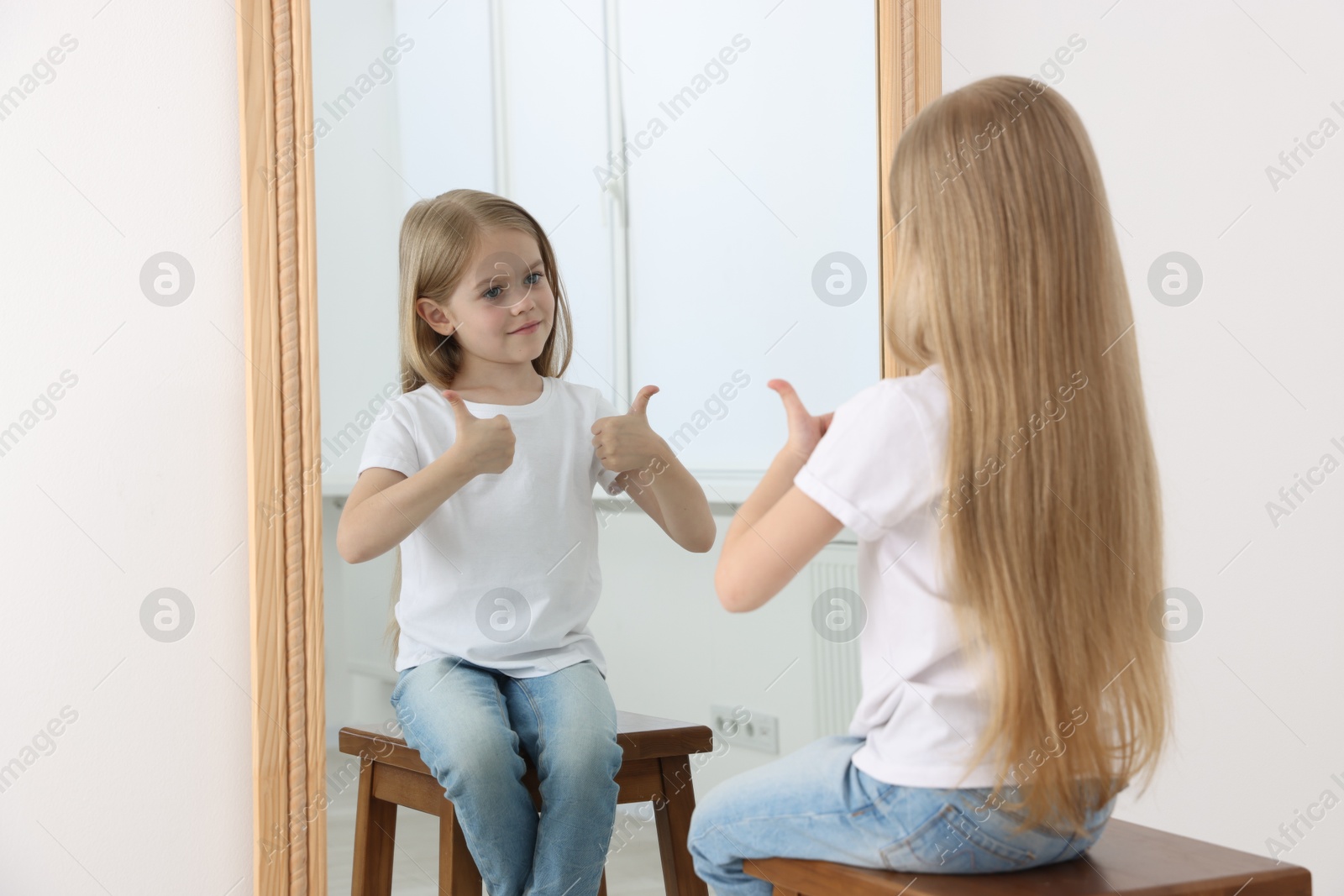 Beautiful little girl showing thumbs up while looking in mirror indoors Photo of Beautiful little girl showing thumbs up while looking in mirror indoors