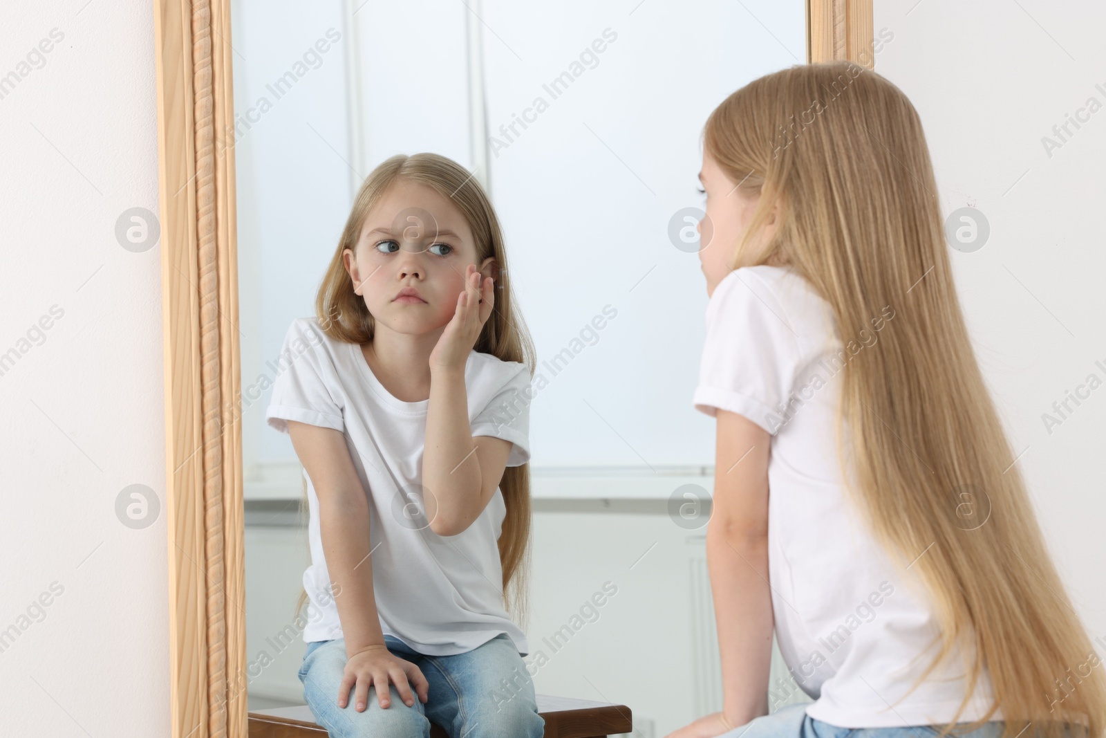 Upset little girl looking at herself in mirror indoors Photo of Upset little girl looking at herself in mirror indoors