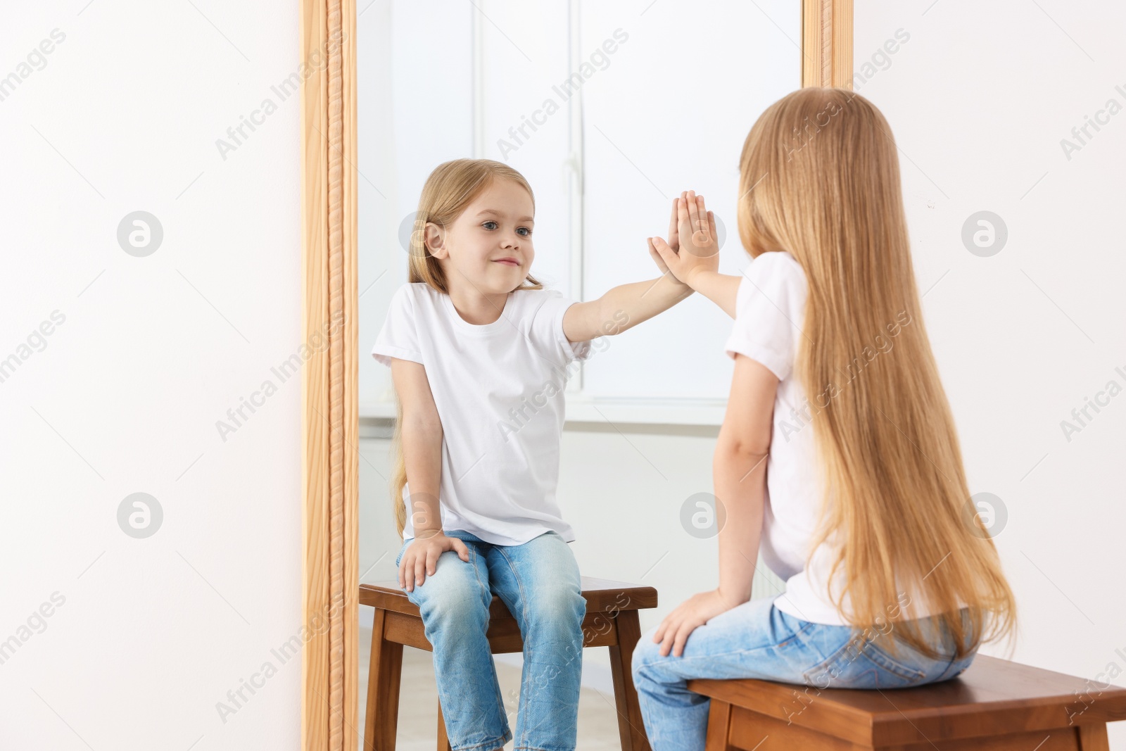 Beautiful little girl looking at herself in mirror indoors Photo of Beautiful little girl looking at herself in mirror indoors