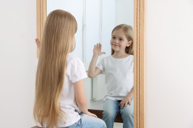 Photo of Beautiful little girl waving while looking in mirror indoors