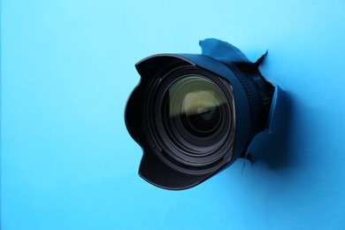 Photo of Hidden camera lens through torn hole in light blue paper
