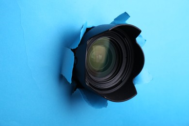 Photo of Hidden camera lens through torn hole in light blue paper