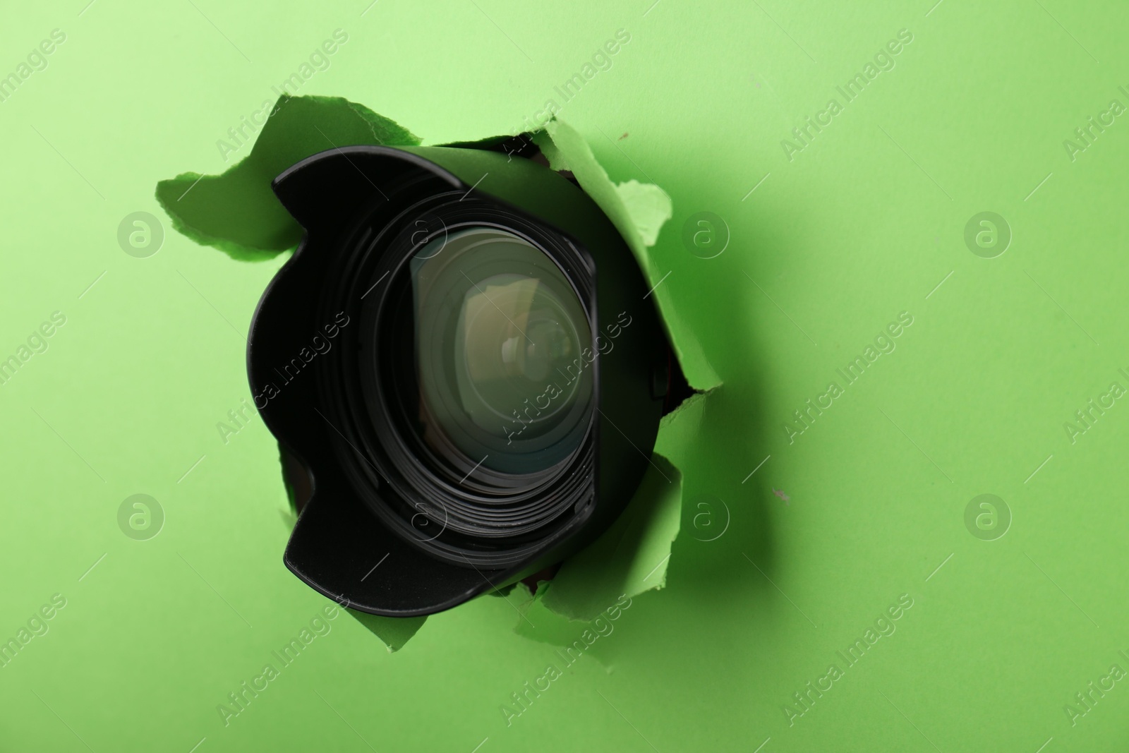 Hidden camera lens through torn hole in green paper Photo of Hidden camera lens through torn hole in green paper
