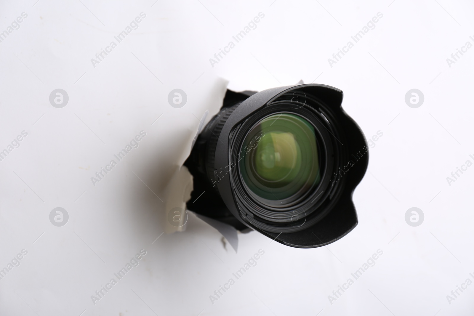 Hidden camera lens through torn hole in white paper Photo of Hidden camera lens through torn hole in white paper