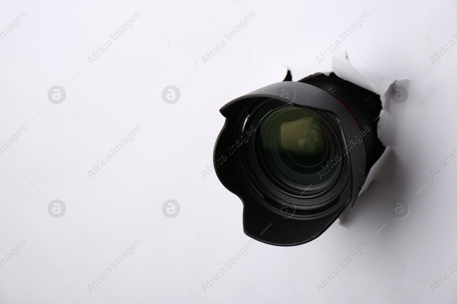 Hidden camera lens through torn hole in white paper. Space for text Photo of Hidden camera lens through torn hole in white paper. Space for text
