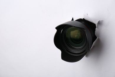 Photo of Hidden camera lens through torn hole in white paper. Space for text