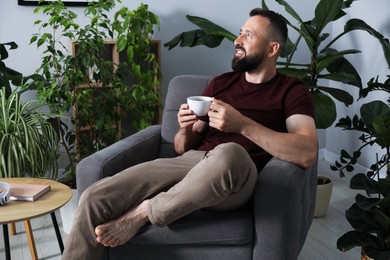 Photo of Harmony. Man with cup of drink in armchair at home