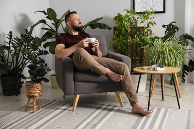 Photo of Harmony. Man with cup of drink in armchair at home