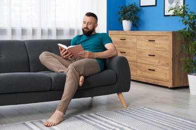 Photo of Harmony. Man reading book on sofa at home
