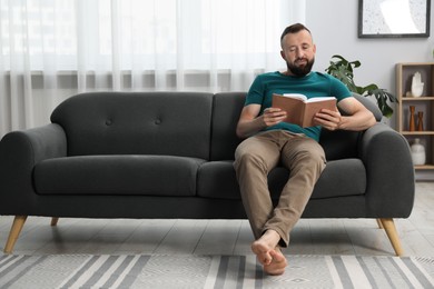 Photo of Harmony. Man reading book on sofa at home