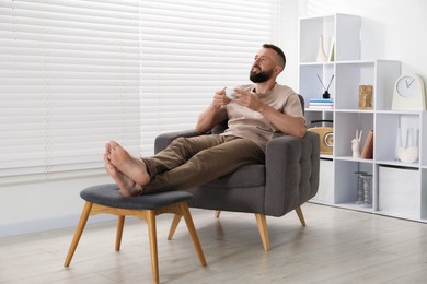 Photo of Harmony. Man with cup of drink in armchair at home