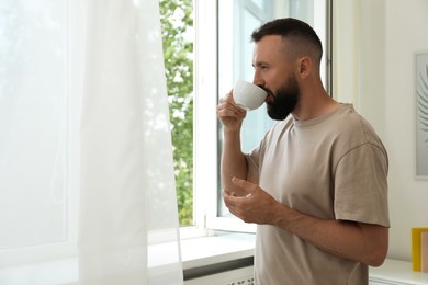 Photo of Harmony. Man drinking tea near window at home