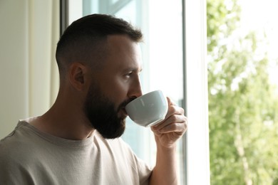 Photo of Harmony. Man drinking tea near window at home