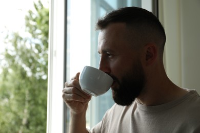 Photo of Harmony. Man drinking tea near window at home
