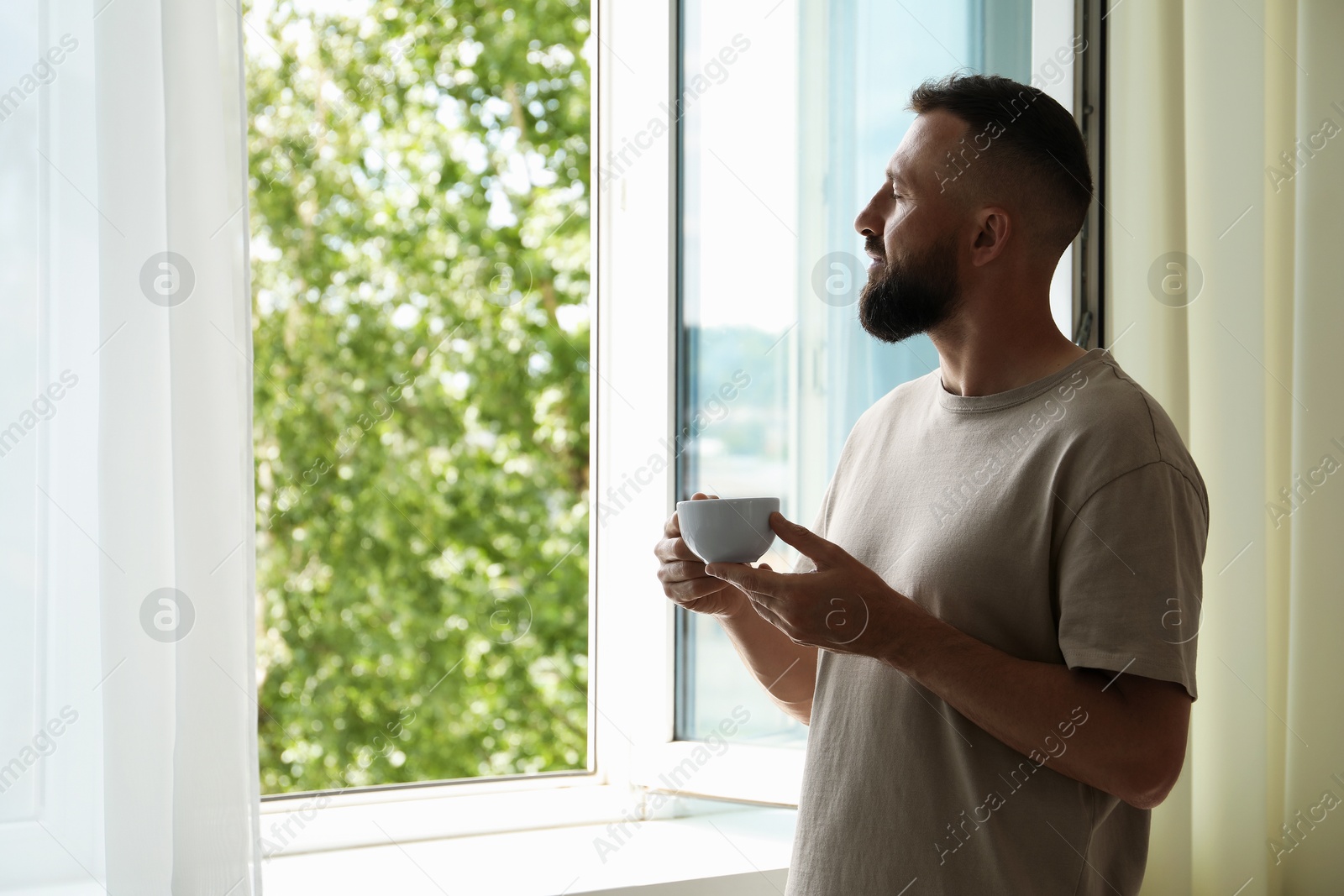 Harmony. Man with cup of drink near window at home Photo of Harmony. Man with cup of drink near window at home
