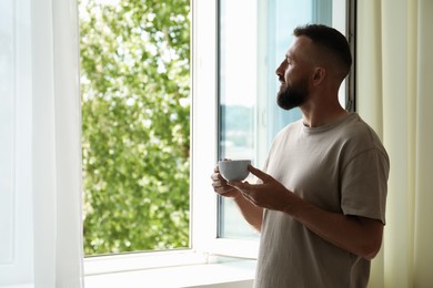 Photo of Harmony. Man with cup of drink near window at home