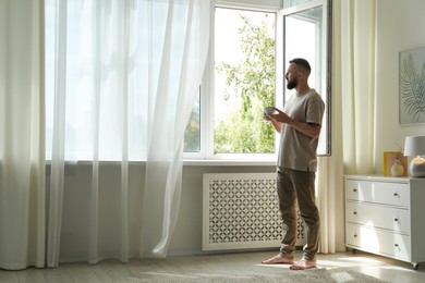Photo of Harmony. Man with cup of drink near window at home