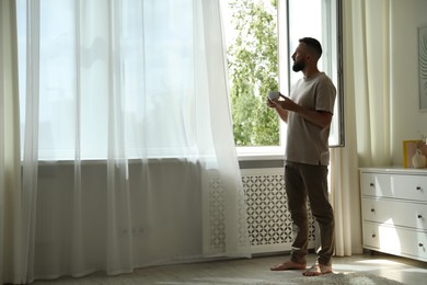 Photo of Harmony. Man with cup of drink near window at home