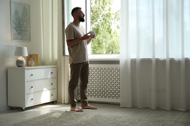 Photo of Harmony. Man with cup of drink near window at home